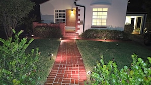 Uma casa com um caminho de tijolos que leva à entrada, cercada por vegetação.
