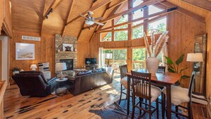 Ein geräumiges Wohnzimmer mit Kamin aus Stein, Holzbalkendecke und großen Fenstern.