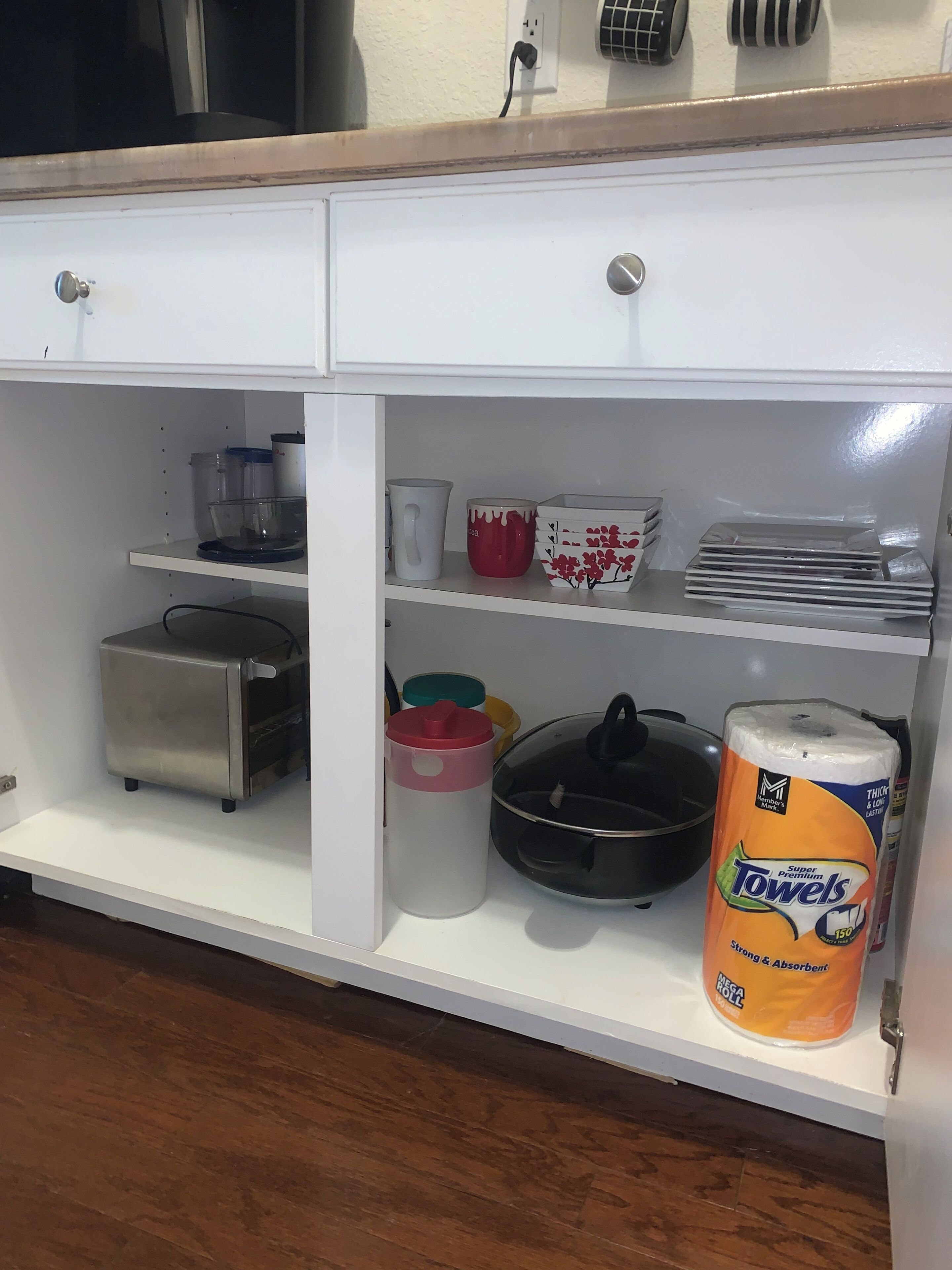 Een keuken met een wit kastje, een roestvrijstalen toaster, een zwarte koekenpan, een rode mok, een witte mok, een rode en witte container, een gele container, een witte container, en een rol Mega Roll handdoeken.