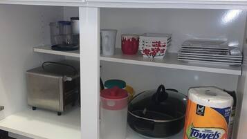 Een keuken met een wit kastje, een roestvrijstalen toaster, een zwarte koekenpan, een rode mok, een witte mok, een rode en witte container, een gele container, een witte container, en een rol Mega Roll handdoeken.