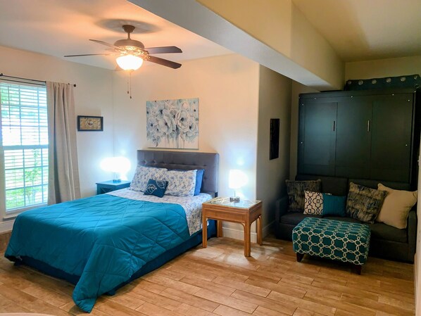 A bedroom with a bed, nightstands, a ceiling fan, a window with curtains, a dark wardrobe, and a patterned ottoman. - Cozy Private Room-Queen&Full Bed, Hot Tub Pool Pets Welcome! (Milton)