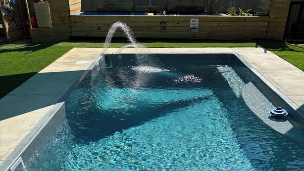 A swimming pool with a water feature, surrounded by a concrete deck.