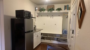 A compact kitchen with a black refrigerator, white cabinets, and a wooden chair.