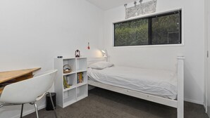 Una habitación pequeña y blanca con una cama individual, un escritorio y una estantería.
