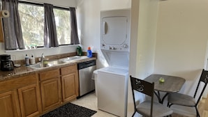 A compact kitchen with wooden cabinets, a built-in dishwasher, a white refrigerator, and a dining area with two chairs and a table.