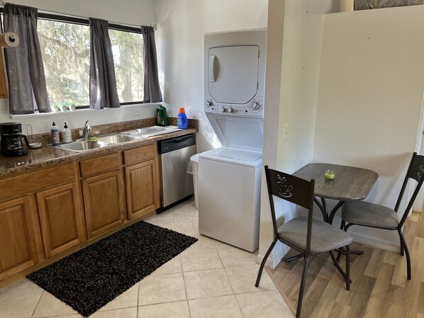 A compact kitchen with wooden cabinets, a built-in dishwasher, a white refrigerator, and a dining area with two chairs and a table.