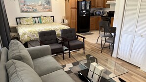 A modern living room with a sofa, two armchairs, a glass coffee table, and a kitchen in the background.