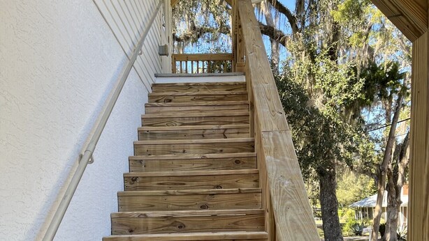 A wooden staircase with a handrail, leading to a covered porch area.