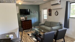 A compact living space with a sofa, chairs, a coffee table, a TV, a dresser, and a clock on the wall.