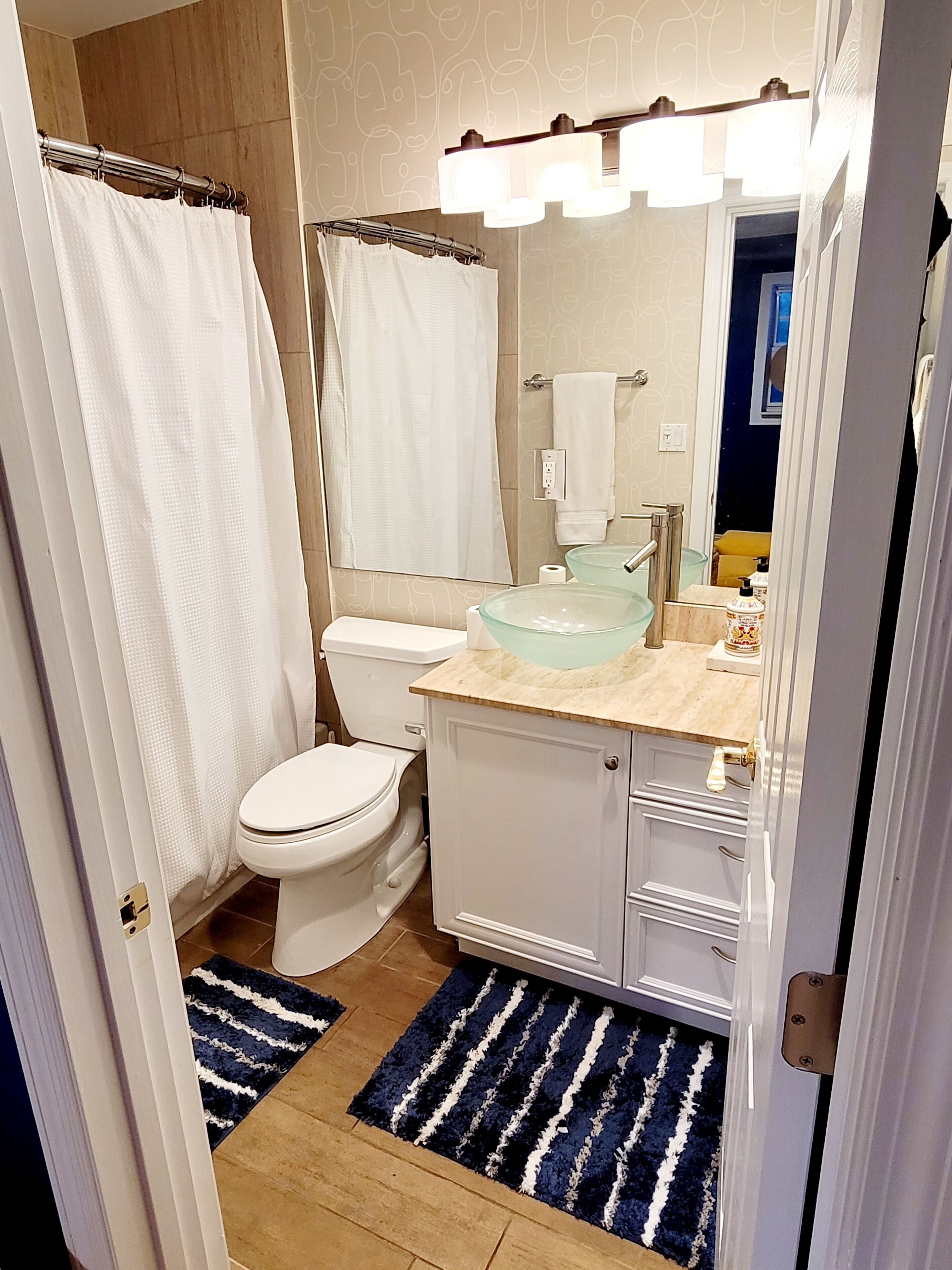Une salle de bain comprenant des toilettes, un lavabo en verre, un miroir et un rideau de douche.
