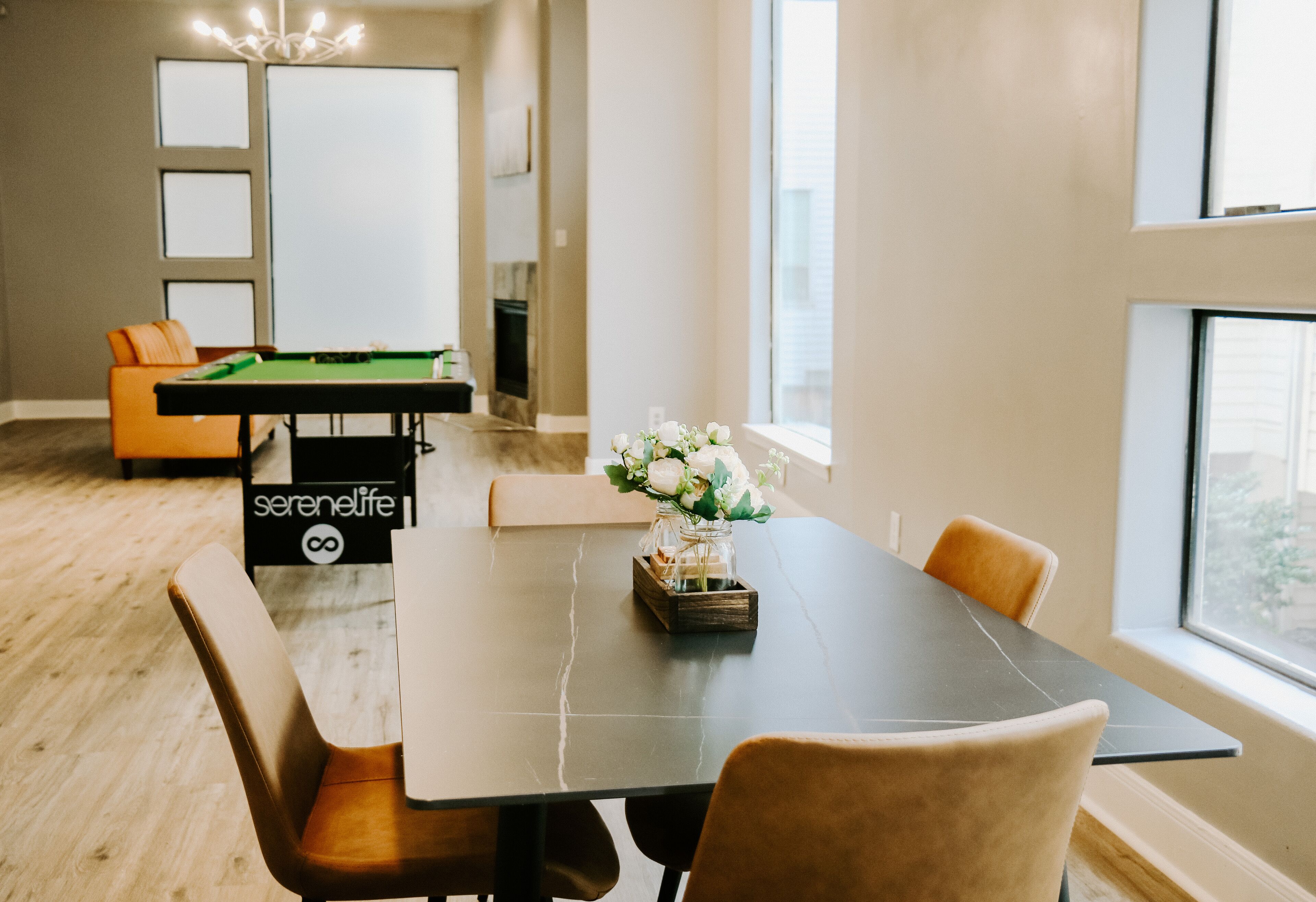 A modern interior with a pool table, a dining table with chairs, and a view of the outdoors.