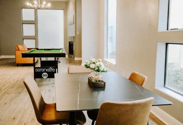 A modern living room with a pool table, comfortable seating, and a large window providing natural light.
