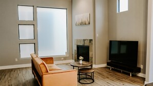 Ein Wohnzimmer mit Sofa, Fernseher, Kamin und großen Fenstern.