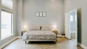 Ein Schlafzimmer mit einem großen Bett, zwei Nachttischen, einer Wandleuchte und einer Tür zu einem Badezimmer.