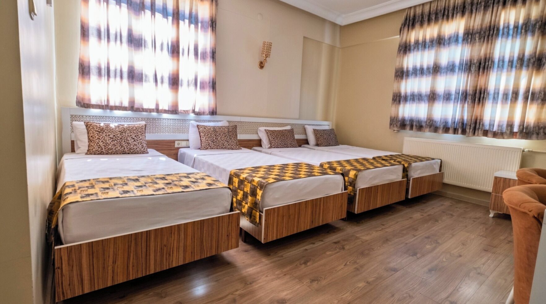 Quarto de hotel com quatro camas simples, piso de madeira, radiador e janela com cortinas.