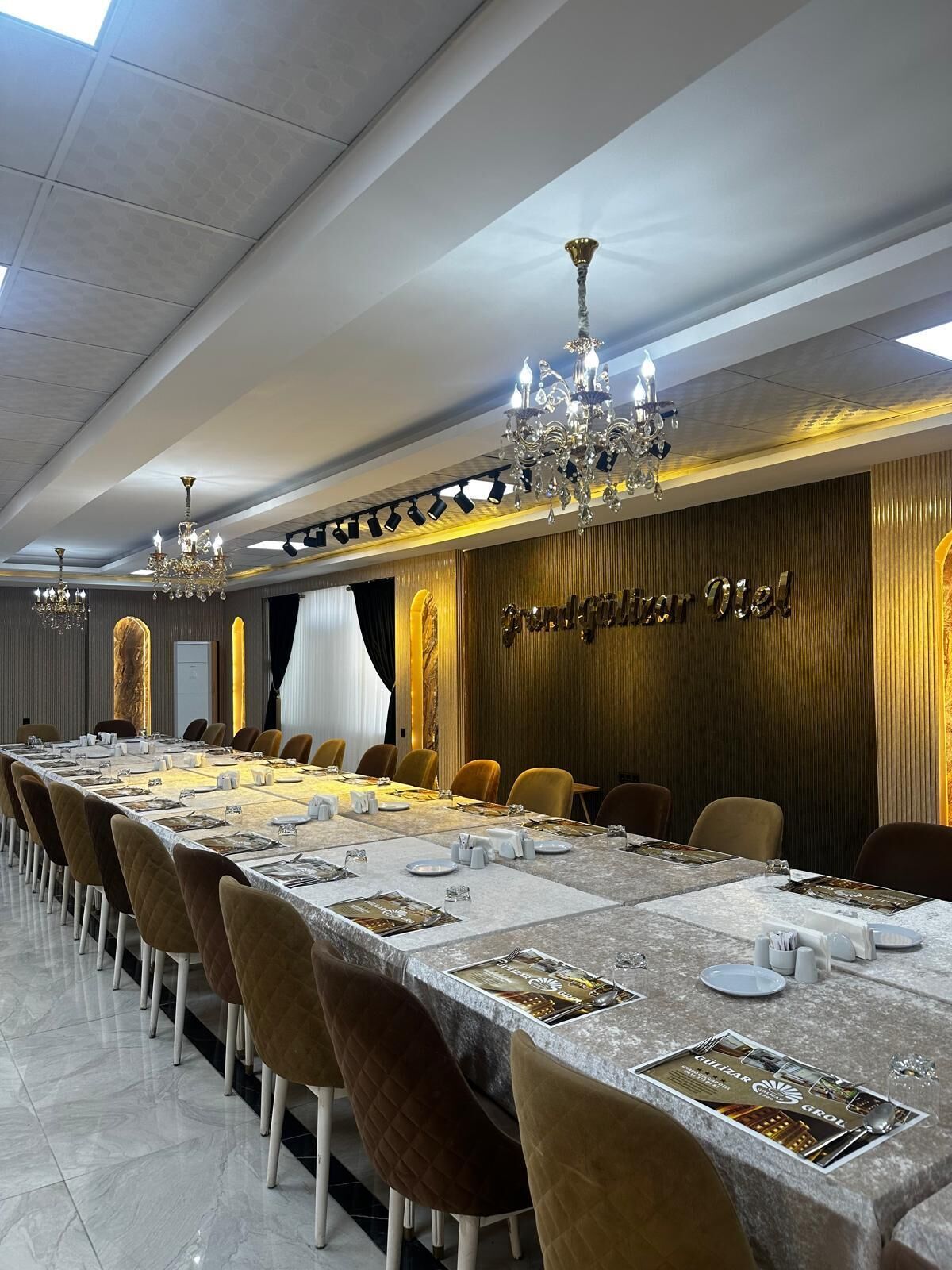 A conference room with a long table, chairs, chandeliers, and a wall with a sign.