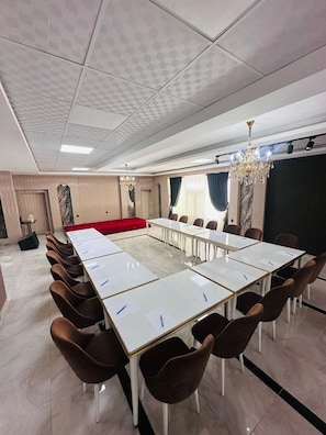 A conference room with a long table, brown chairs, a red sofa, a chandelier, and a large screen. - Grand Gulizar Hotel (Sanliurfa)