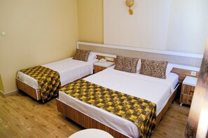Habitación de hotel con dos camas individuales, suelo de madera, pared blanca y mesita de noche con lámpara.