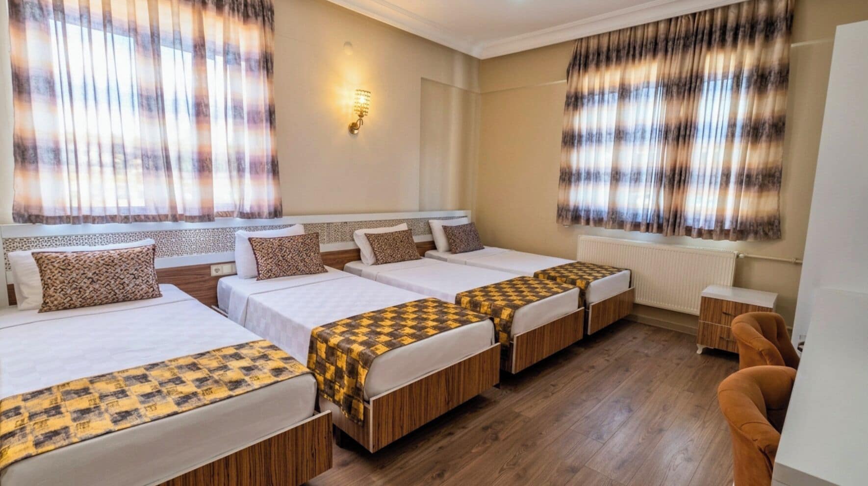 A hotel room with four beds, a wooden floor, a radiator, and a small wooden side table.
