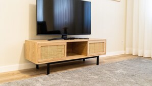 Un televisor de pantalla plana sobre un mueble de madera con panel frontal tejido, ubicado frente a una pared con un cuadro enmarcado.