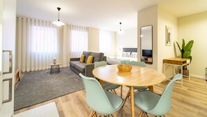 Una sala de estar moderna con una mesa redonda de madera, sillas azul claro, un sofá gris y un espejo grande en la pared.