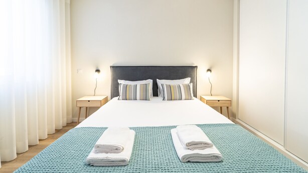 Una habitación de hotel con una cama, dos mesitas de noche, cabecero, cortinas y una alfombra azul con textura.