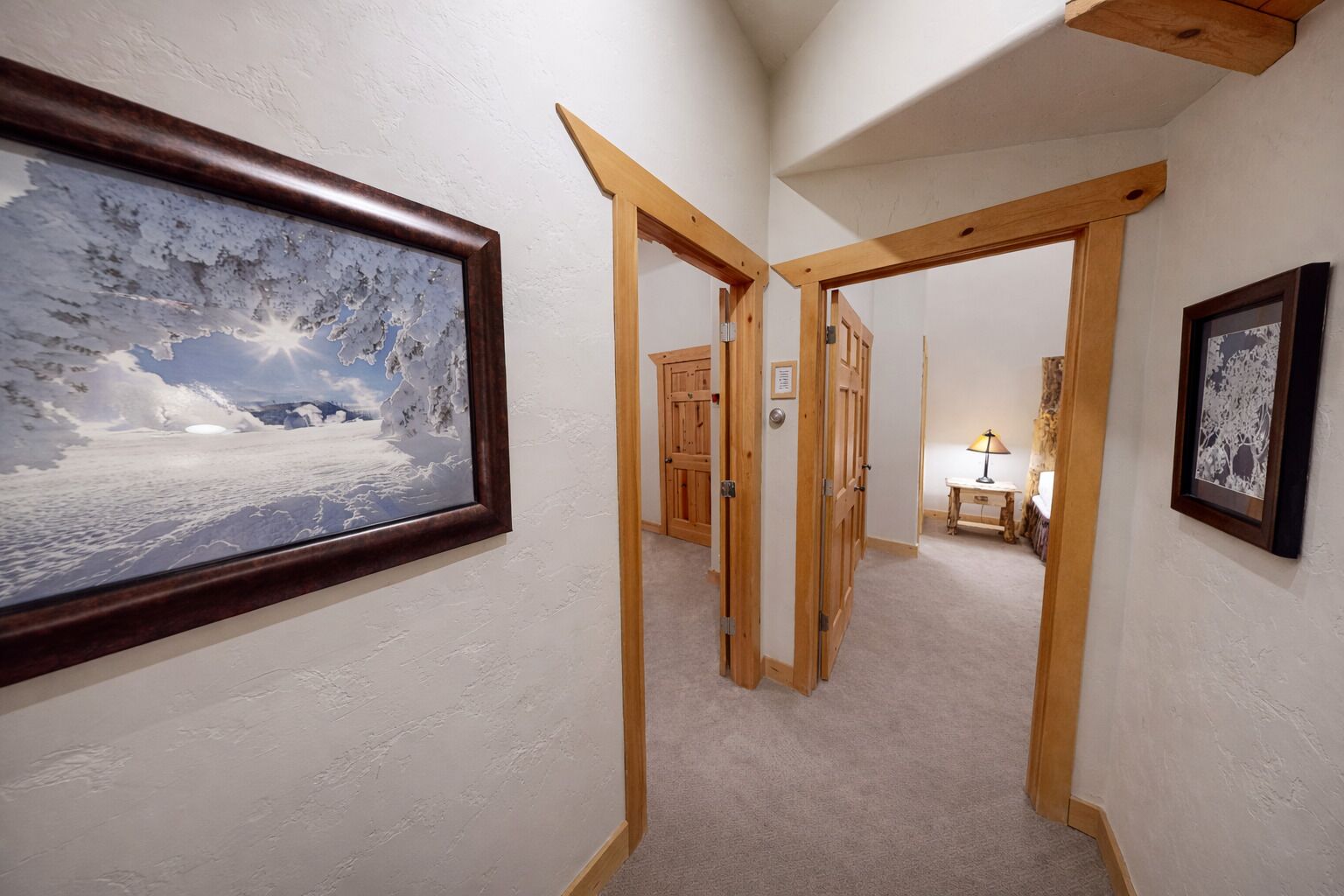 Ein Flur mit Holztüren, einem gerahmten Bild einer verschneiten Landschaft und einem kleinen Tisch mit einer Lampe.