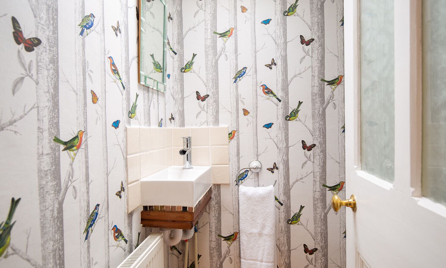 A bathroom with a white sink, a mirror, and a towel rack. The walls are decorated with a bird and butterfly pattern.