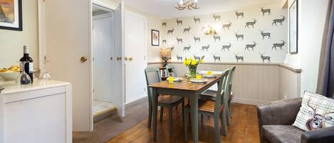 A dining area with a wooden table set for four, surrounded by chairs. A chandelier hangs from the ceiling, and the walls are decorated with a pattern of deer silhouettes.