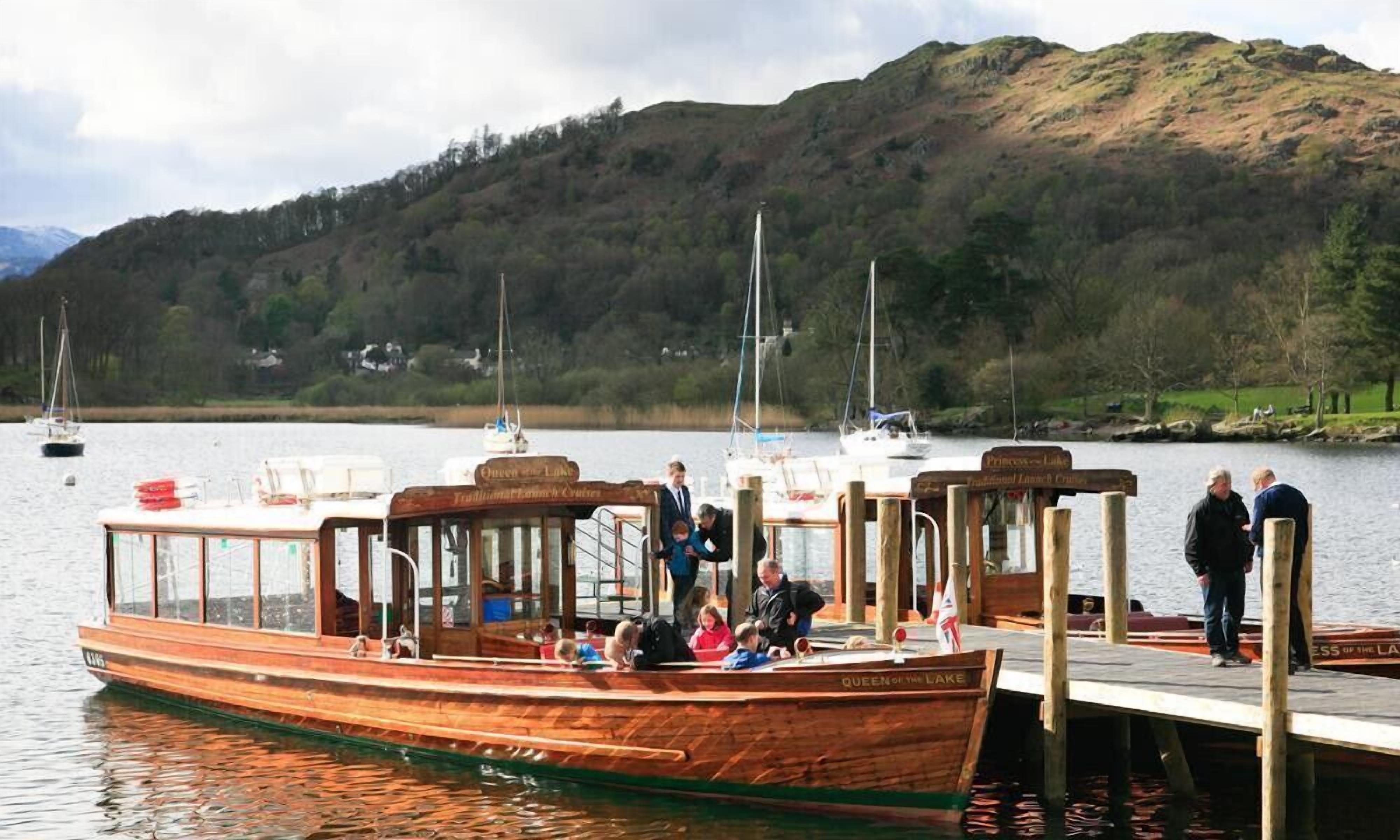 A wooden boat docked at a pier with people on board and a mountainous landscape in the background.