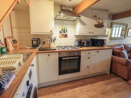 A compact kitchen with a gas stove, oven, and microwave. There is a wooden countertop, a sink, and a dining area with a brown leather couch.