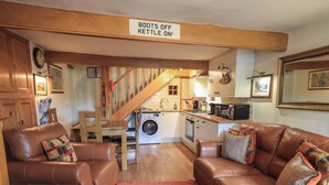 A cozy living room with leather sofas, a red rug, and a sign indicating kettles are on. - Heron Cottage (Ambleside)
