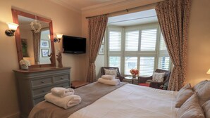 A hotel room with a large bed, a dresser, a television, and a window with curtains. - Heron Cottage (Ambleside)