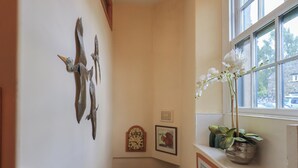 A corner of a room with a clock, framed pictures, and a window with a plant. - Heron Cottage (Ambleside)