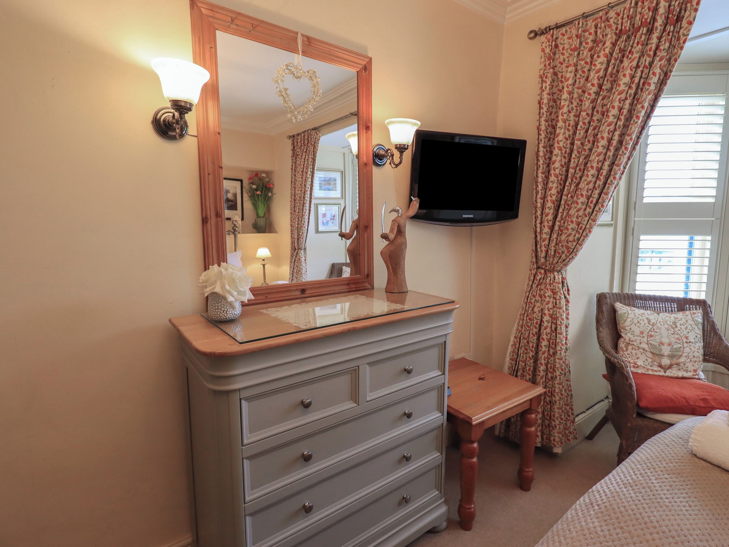 A bedroom with a dresser, a television, a chair, and a window with curtains.