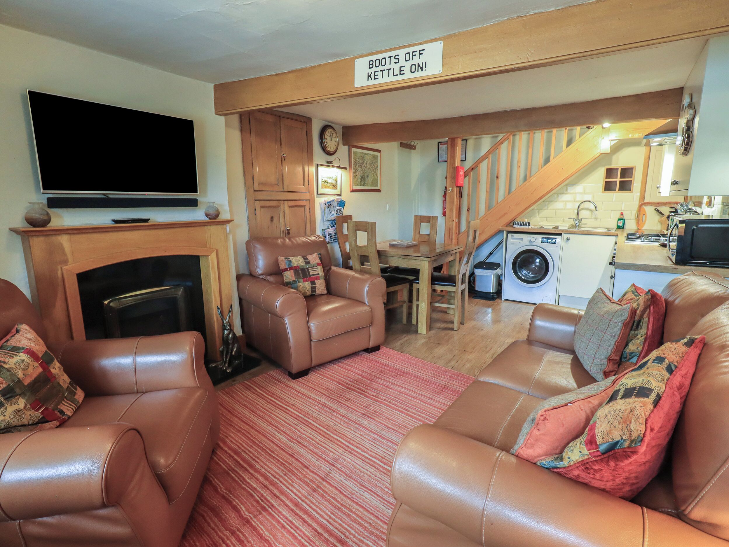 Una sala de estar acogedora con sofás de cuero, chimenea, televisión y una zona de cocina con cartel de tetera.