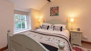 A bedroom with a bed, bedside tables, a window, and a painting on the wall. - Swinside Cottage (Keswick)