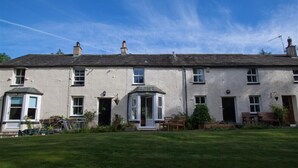 A two-story building with a flat roof, multiple windows, and a small porch area with chairs. - Swinside Cottage (Keswick)