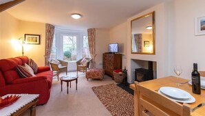 A cozy living room with a red sofa, two armchairs, a small table, a fireplace, and a dining area with a table and chairs. - Swinside Cottage (Keswick)