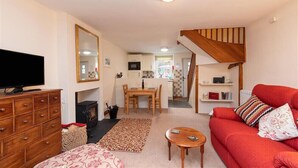 A cozy living room with a TV, wooden dresser, red sofa, and a staircase. - Swinside Cottage (Keswick)