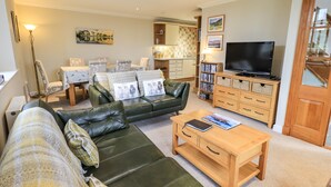 A living room with a green sofa, a wooden coffee table, a TV, and a bookshelf. - Middlerigg (Windermere)