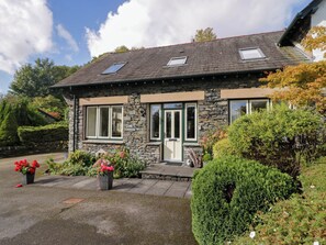 A stone house with a sloped roof, two windows with shutters, and a small porch area. - Middlerigg (Windermere)