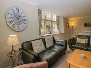 A living room with a large wall clock, a sofa, a coffee table, and a lamp. - Middlerigg (Windermere)