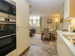 A kitchen with a built-in oven, a dining area with a table and chairs, and a view of the outdoors through a window. - Middlerigg (Windermere)