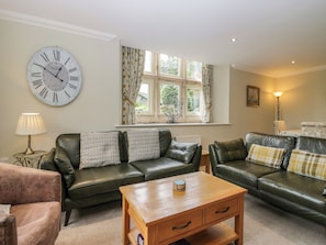 A living room with leather sofas, a wooden coffee table, a large wall clock, and a window with curtains. - Middlerigg (Windermere)