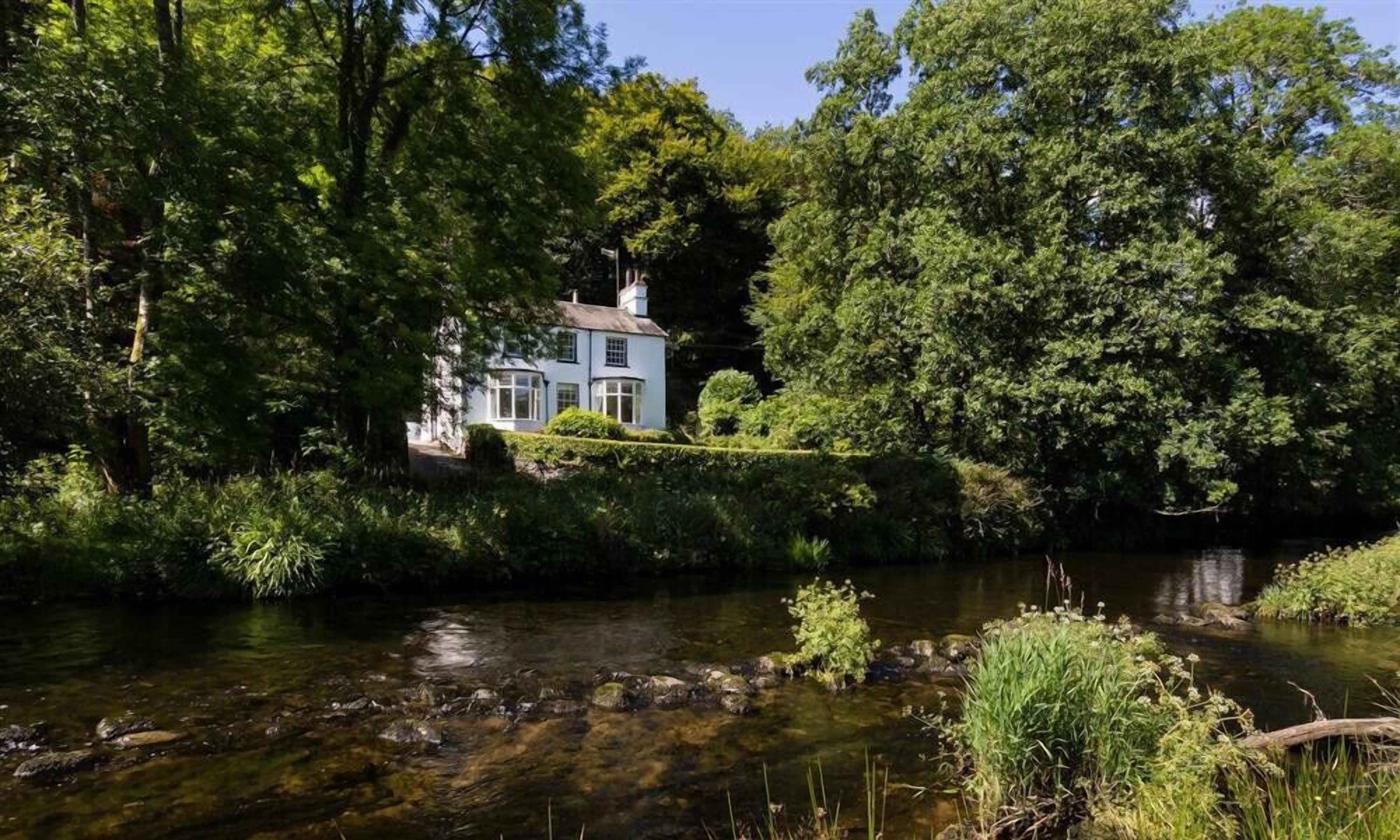 A house with a conservatory, surrounded by dense greenery and a river.
