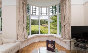 A room with a bay window, a sofa, a glass table, and a flat-screen TV.