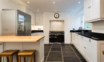 A modern kitchen with white cabinets, a black stove, and a wooden island with stools.