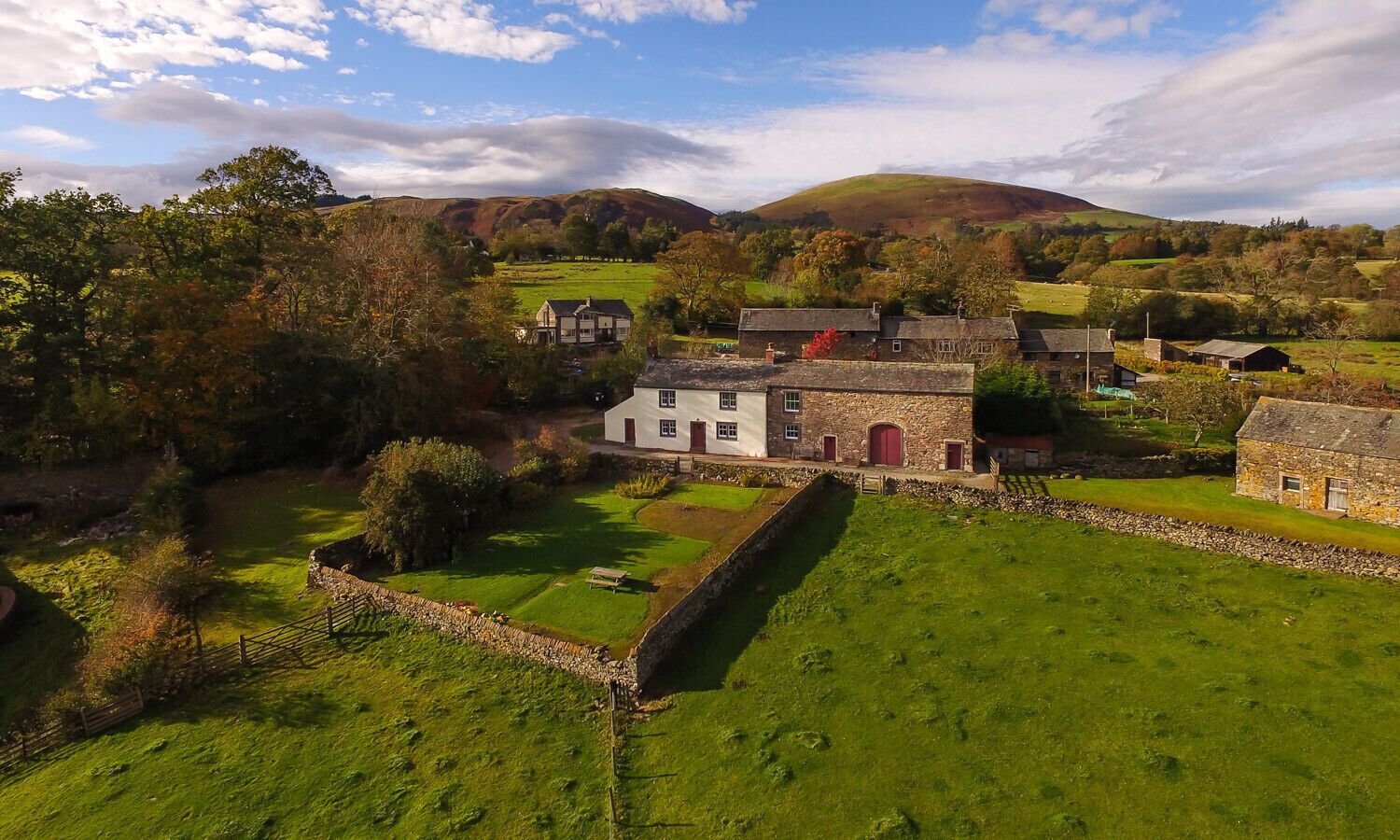 A rural landscape with stone buildings, a stone wall, and a grassy field.
