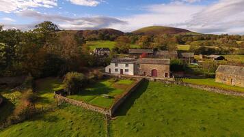 A rural landscape with stone buildings, a stone wall, and a grassy field.